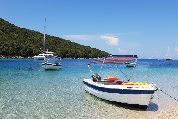 Μικρές βάρκες και ένα καταμαράν αγκυροβολημένο από μια αμμώδη παραλία με γαλαζοπράσινα νερά.