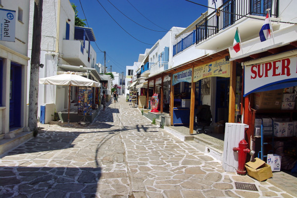 Ένας κεντρικός λιθόστρωτος δρόμος στο νησί της Αντιπάρου με καταστήματα και στις δύο πλευρές.