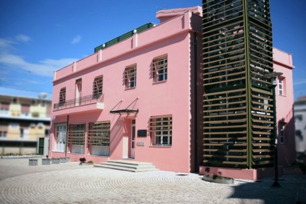 Η Δημοτική Πινακοθήκη Άρτας - Γ. Μόραλης είναι ένα διώροφο ροζ κτίριο με καλυμμένη εξωτερική σκάλα.