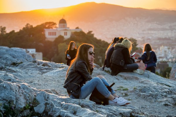 Ένα κορίτσι καπνίζει και φίλες συνομιλούν στον λόφο του Αρεοπάγου τη στιγμή του ηλιοβασιλέματος.