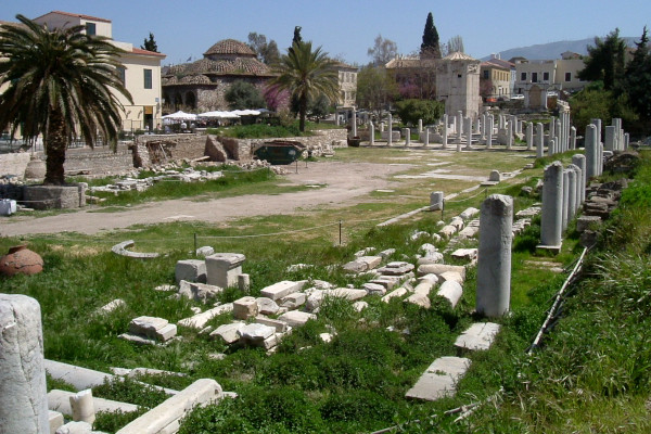 Λευκές στήλες και άλλα κατάλοιπα της Ρωμαϊκής Αγοράς της Αθήνας απλώνονται τριγύρω πάνω σε γρασίδι. 