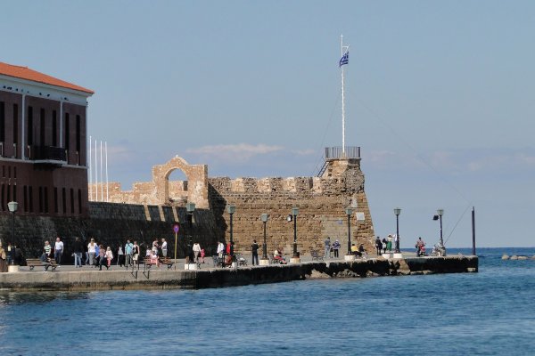 Τα πέτρινα τείχη του ενετικού φρουρίου Φιρκά δίπλα στη θάλασσα και τουρίστες που κάνουν βόλτα.