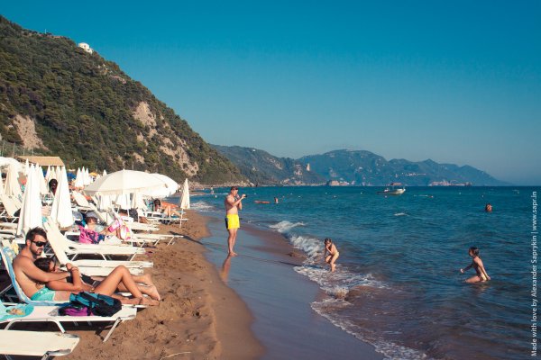 Κόσμος απολαμβάνει τη θάλασσα και τον ήλιο στην αμμώδη παραλία της Γλυφάδας στην Κέρκυρα.