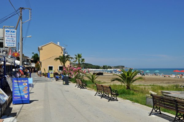 Ένας δρόμος με παγκάκια στη μία πλευρά και εστιατόρια στην άλλη στην παραλία Ρόδα, Κέρκυρα.