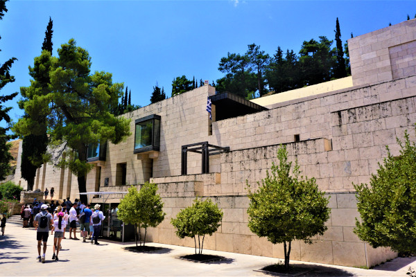 Η μπροστινή πλευρά του Αρχαιολογικού Μουσείου Δελφών με μερικούς επισκέπτες να πλησιάζουν την κύρια είσοδο.