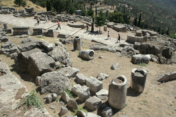 Πανοραμική θέα της πλακόστρωτης Ιερής Οδού στους Δελφούς γεμάτης με κατεστραμμένους κίονες και ερείπια.