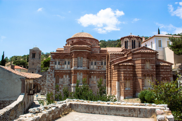 Το βυζαντινό μοναστήρι του Οσίου Λουκά χτισμένο με καφέ και λευκή πέτρα κάτω από το γαλάζιο του ουρανού.