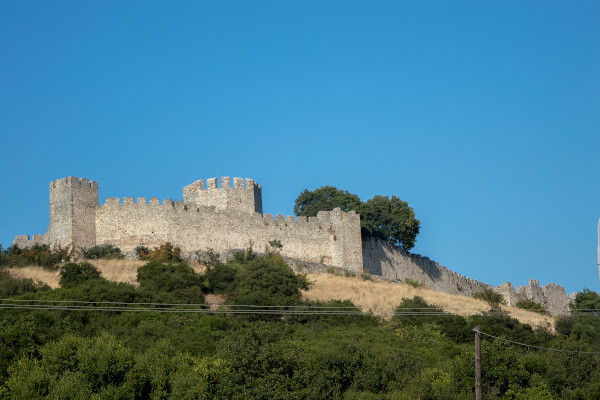 Τα τείχη του κάστρου του Πλαταμώνα ανάμεσα στην πυκνή βλάστηση και το γαλάζιο του ουρανού στο βάθος.