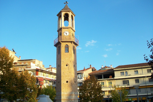 Ο πύργος ρολογιού των Γρεβενών με φόντο κτίρια της πόλης καθώς και τον γαλάζιο ουρανό.
