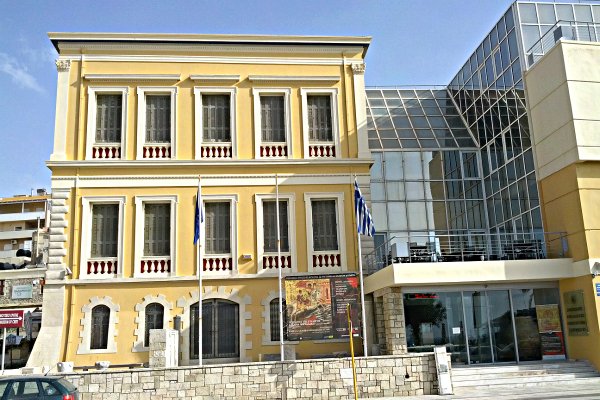 Ένα κίτρινο νεοκλασικό κτίριο και ένα σύγχρονο κτίριο από γυαλί και χάλυβα στο Ιστορικό Μουσείο Κρήτης.