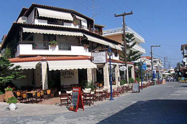 Ένας κεντρικός δρόμος της Χανιώτης με εστιατόρια, καφετέριες και υπαίθρια καθίσματα στο πεζοδρόμιο.