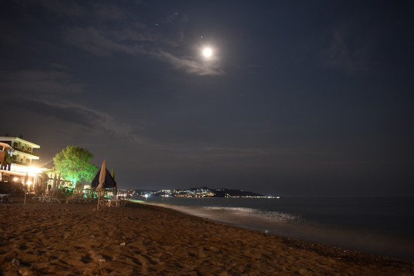 Μια νυχτερινή λήψη που δείχνει την παραλία της Σκάλας Φούρκας στη Χαλκιδική κάτω από το φως του φεγγαριού.