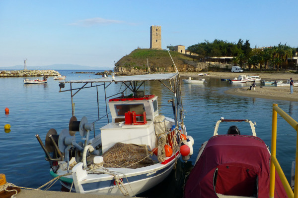 Το λιμάνι της Νέας Φώκαιας με μικρά ψαροκάικα και ο λόφος με φόντο τον Βυζαντινό Πύργο του Αγίου Παύλου.