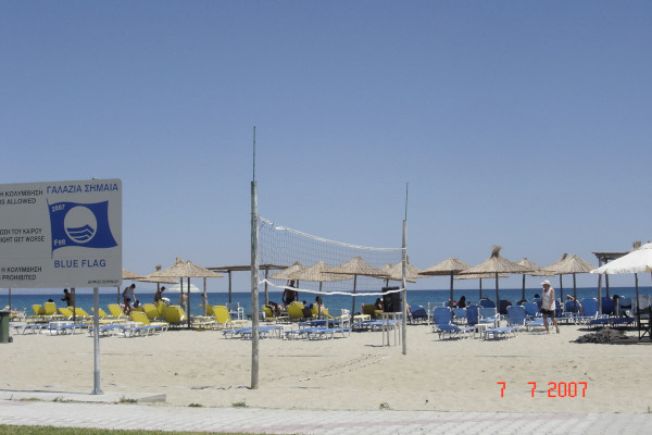 Ένα γήπεδο beach volley, μια ταμπέλα με γαλάζια σημαία και πολλές ομπρέλες και ξαπλώστρες στην παραλία Κορινός της Κατερίνης.