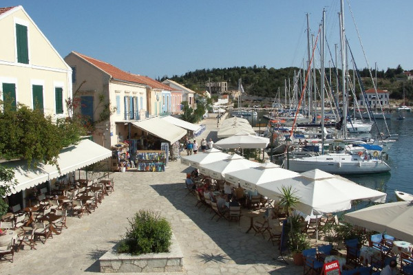 Μαγαζιά και εστιατόρια στον παραλιακό πεζόδρομο του Φισκάρδου και πολλά ιστιοφόρα αγκυροβολημένα στο λιμάνι.