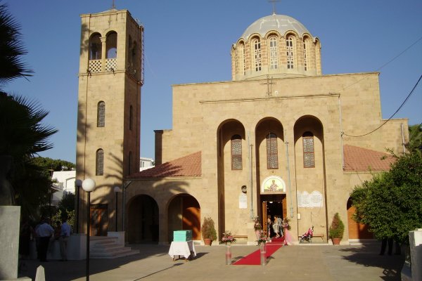 Μια ανοιχτόχρωμη ογκώδης εκκλησία με κόκκινο χαλί που οδηγεί στην είσοδό της και ένα καμπαναριό.