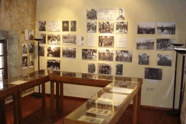 Μια αίθουσα του Μουσείου με εκθέματα σε θήκες και φωτογραφίες να κρέμονται στους τοίχους.