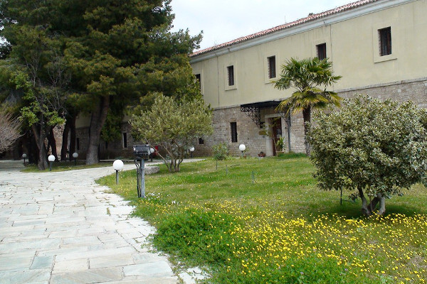 Η κύρια είσοδος του Αρχαιολογικού Μουσείου Λαμίας ανάμεσα σε δέντρα και καταπράσινη βλάστηση.