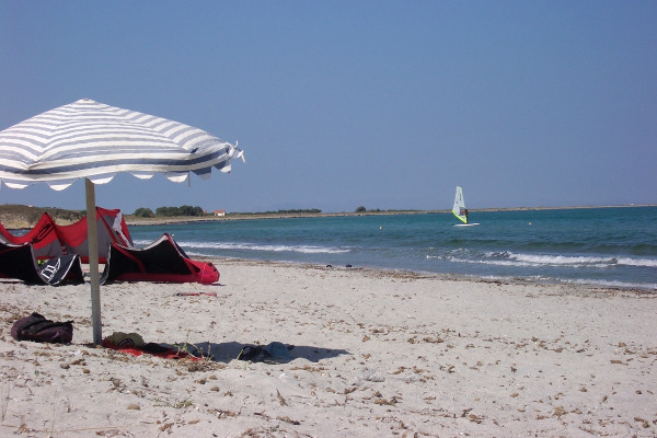Μια φωτογραφία με μια ομπρέλα και έναν windsurfer στο βάθος τραβηγμένη στην παραλία της Κέρου στη Λήμνο.