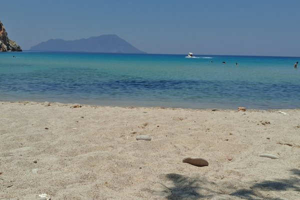 Άμμος στην παραλίας Πλάθιενα, νερά ανάμεικτων πράσινων και μπλε αποχρώσεων και ένα νησί στο βάθος.