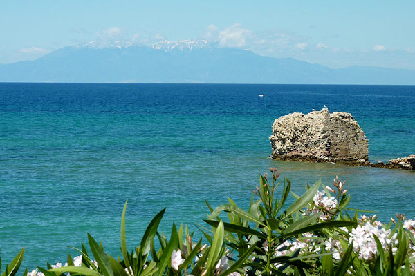 Υπολείμματα  του αρχαίου λιμανιού της Ποτίδαιας, με τη γαλάζια θάλασσα και τον χιονισμένο 'Ολυμπο στο βάθος.