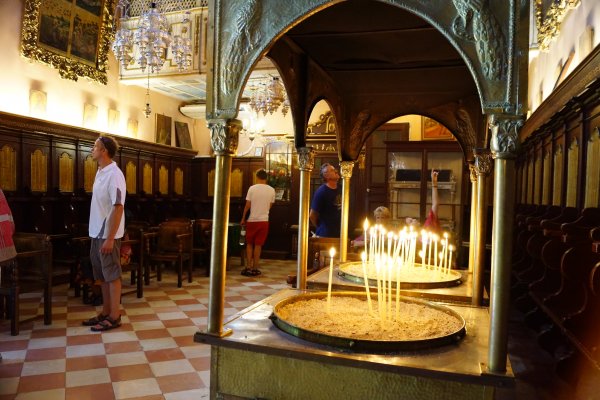 Κεριά καίνε στο μοναστήρι της Παλαιοκαστρίτσας καθώς επισκέπτες περιεργάζονται τη θρησκευτική τέχνη που κοσμεί το ναό.