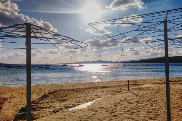 Ομπρέλες χωρίς κάλυμμα σε μια παραλία με χρυσή άμμο και ο ήλιος να αντανακλάται στη θάλασσα .