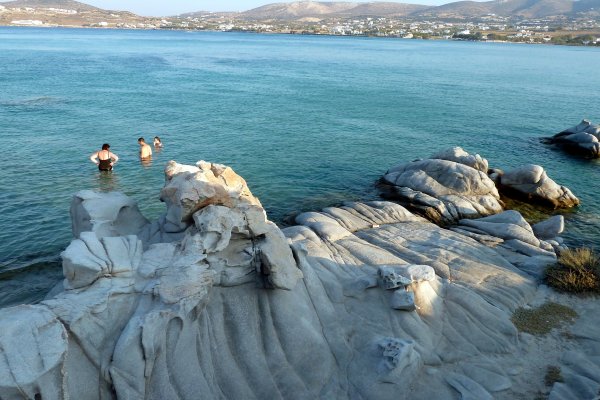 Βράχοι με λεία επιφάνειας σμιλεμένοι από τα κύματα και λίγοι άνθρωποι μέσα στη θάλασσα στην παραλία Κολυμπήθρες, Νάουσα, Πάρος.