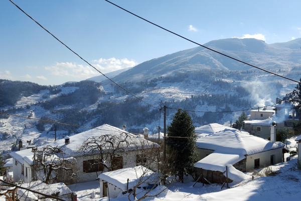 Μερικά από τα χιονισμένα σπίτια της Ζαγοράς στο Πήλιο με το βουνό στο βάθος κατά τη διάρκεια μιας ηλιόλουστης μέρας.