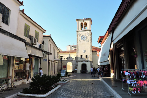 Το ενετικό ρολόι & η εκκλησία του Αγίου Χαραλάμπους Πρέβεζας στο τέλος ενός πεζόδρομου με καταστήματα και μπουτίκ.