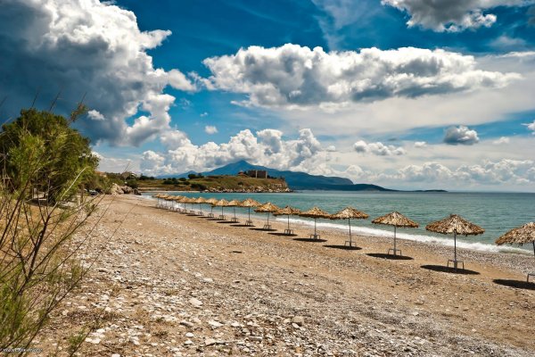 Μια σειρά από ομπρέλες παραλίας δίπλα στη θάλασσα και τους θάμνους, κάτω από έναν συννεφιασμένο ουρανό στο Πυθαγόρειο της Σάμου.