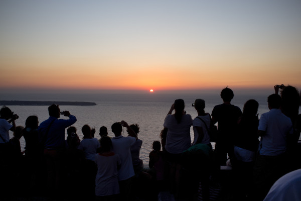 Άνθρωποι που κοιτούν και φωτογραφίζουν το μαγικό ηλιοβασίλεμα στη Σαντορίνη.