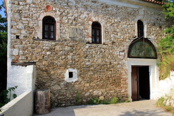 Η είσοδος και ένας καφετής τοίχος από πέτρα στη Μονή Παναγίας Εικονίστριας, Σκιάθος.