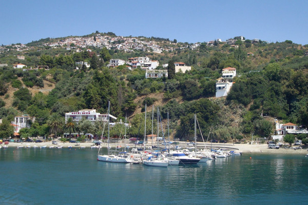Μια φωτογραφία που απεικονίζει ιστιοφόρα αγκυροβολημένα στο λιμάνι του Λουτρακίου, και το χωριό Γλώσσα στην κορυφή του λόφου.