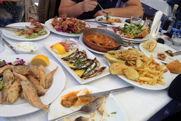 Ένα ταβερνάκι τραπέζι γεμάτο διαφορετικά πιάτα για γεύση ενώ η παρέα πίνει τσίπουρο το ελληνικό απόσταγμα.