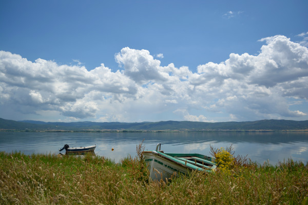 Τα νερά της λίμνης αντανακλούν τον γαλάζιο ουρανό και ένα αλιευτικό σκάφος είναι αραγμένο στην ακτή.