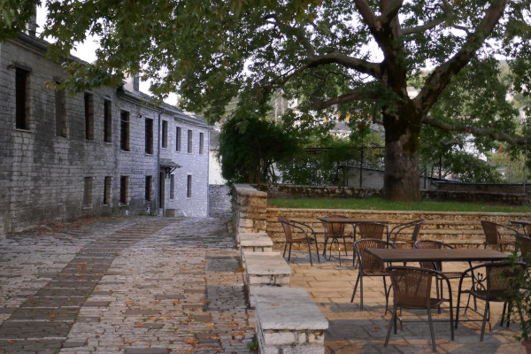 Ένα μέρος της κεντρικής πλατείας της Βίτσας με λιθόστρωτο δρόμο, υπέροχο πλατάνο και τραπέζι με καρέκλες.